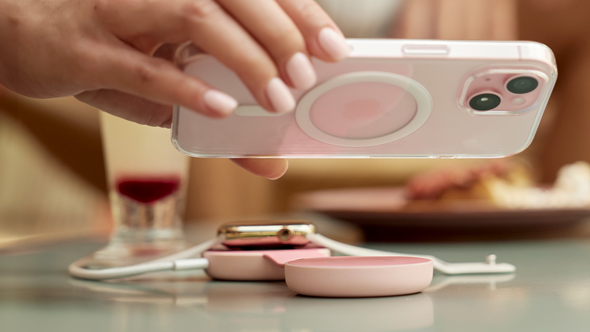 Female hand putting a pink iPhone onto a pink charging mat on a table.